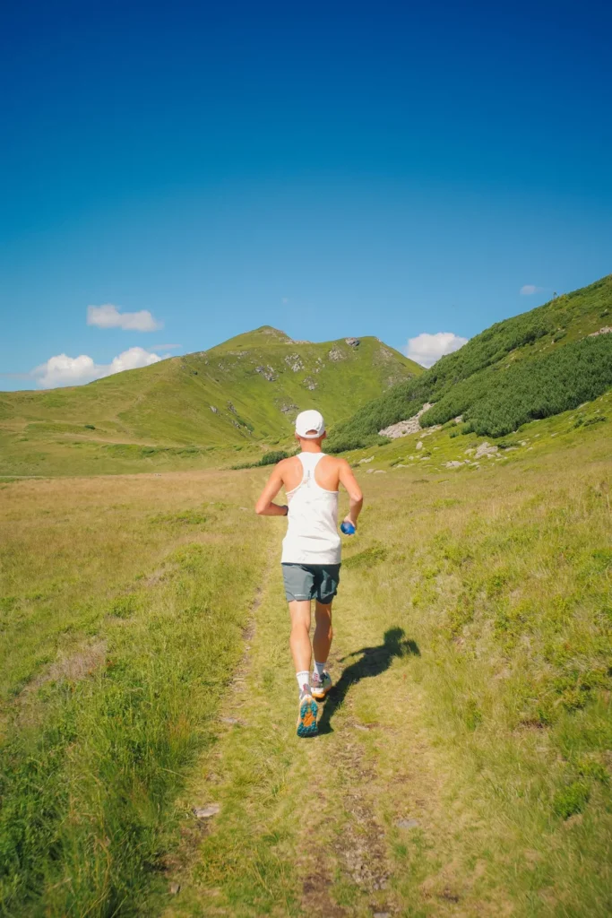 Runner in a sleeveless top following a grassy mountain trail.