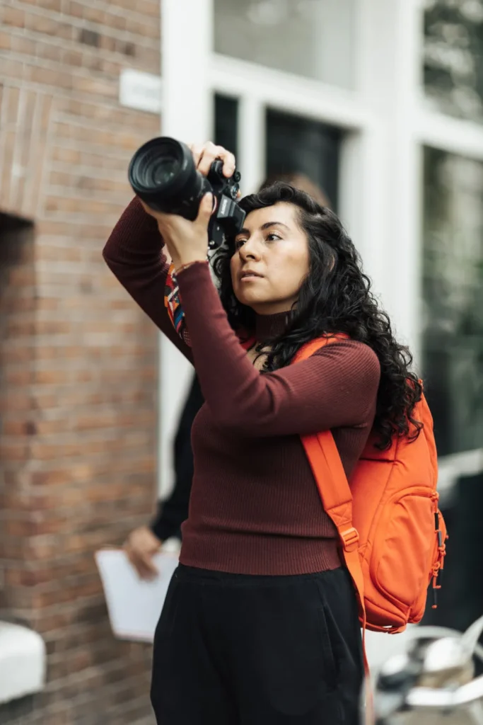 Woman wearing an orange backpack over a burgundy knitted sweater.