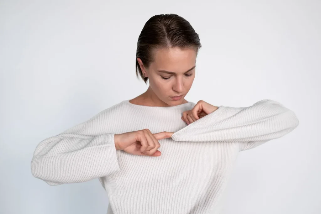 A woman examining the sleeve of a white knitted sweater.