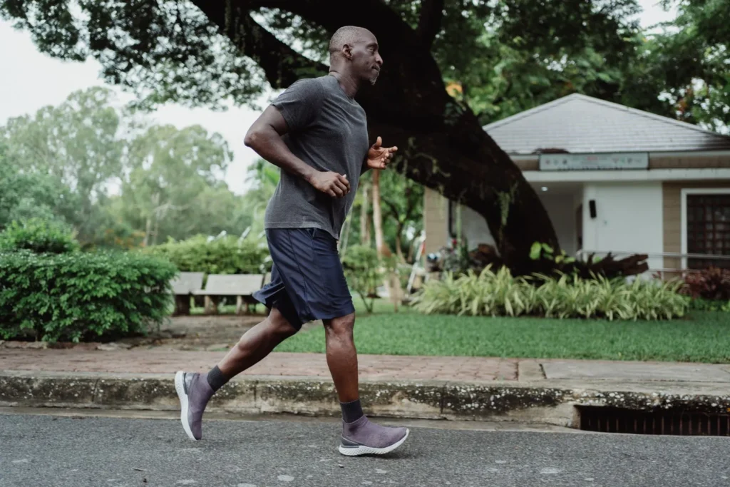 Runner wearing a gray T-shirt and dark shorts on a tree-lined street.