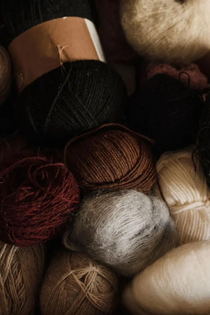 Assorted yarn balls with smooth and fuzzy surface textures in neutral and dark colors.