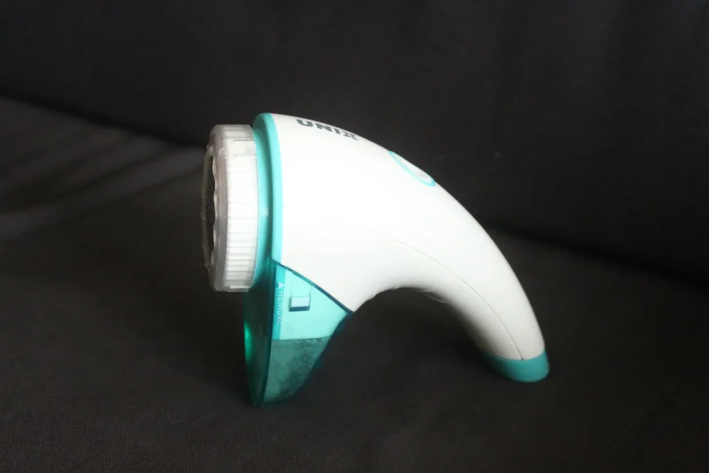 White and turquoise handheld fabric shaver resting on dark fabric.
