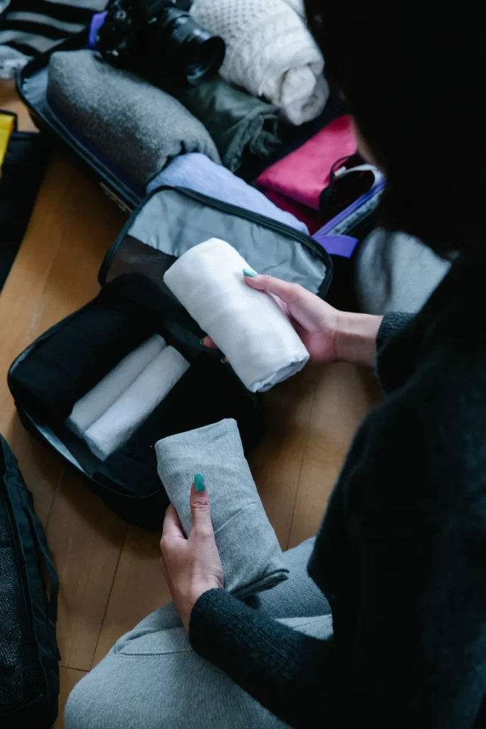 Person organizing rolled and folded clothing in packing cubes beside an open suitcase.