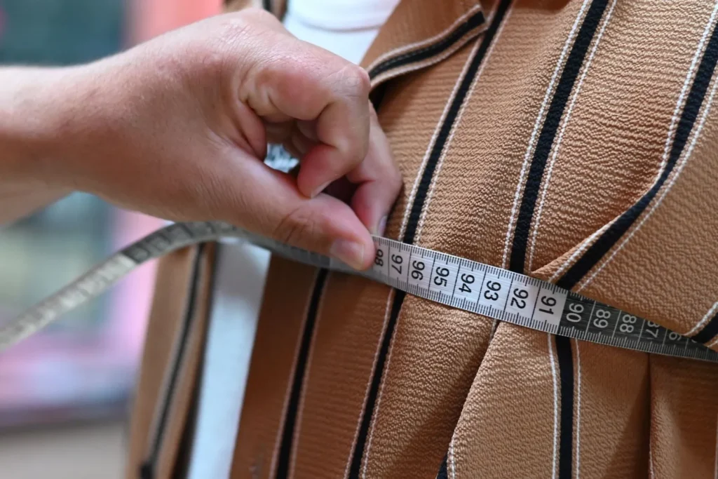 A hand using a tape measure to check the size of a brown striped garment.