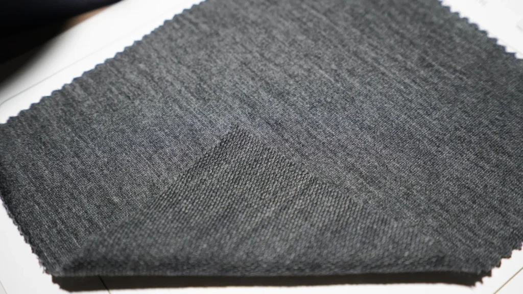 Navy merino wool fabric swatch with a specification label listing 165 GSM and 100 percent merino wool.