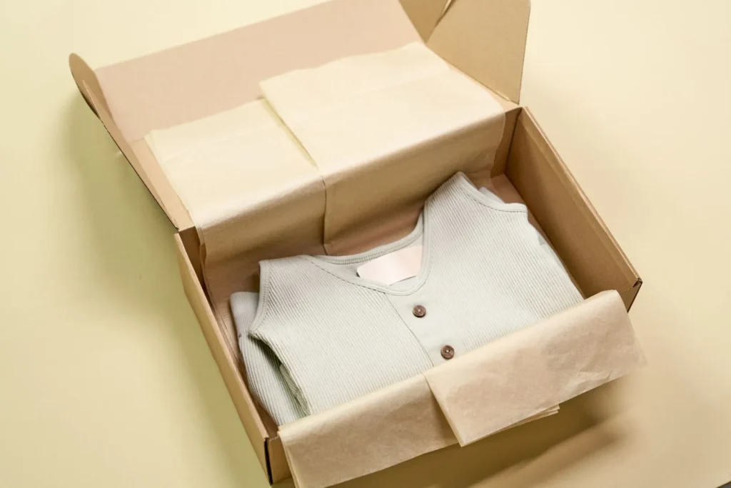 A folded ribbed garment packed in a cardboard box with tissue paper